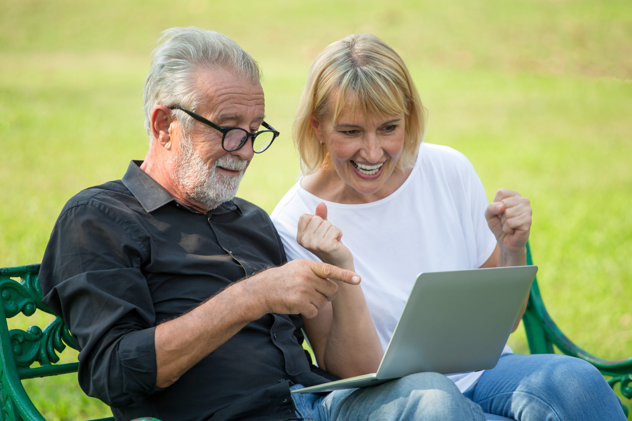 happy senior couple looking at laptop at the park