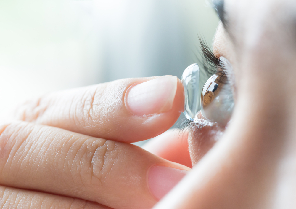 person putting contact lens in eye